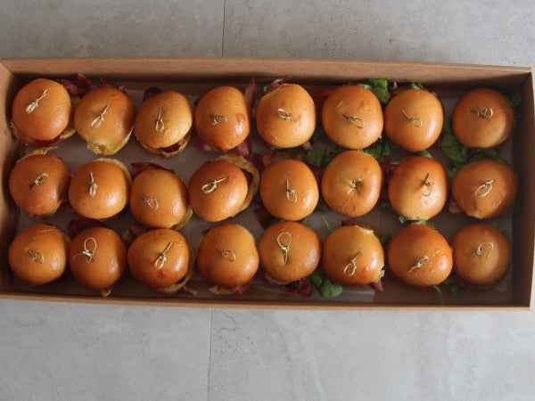 A platter of breakfast sliders with various fillings, presented in a long rectangular box.