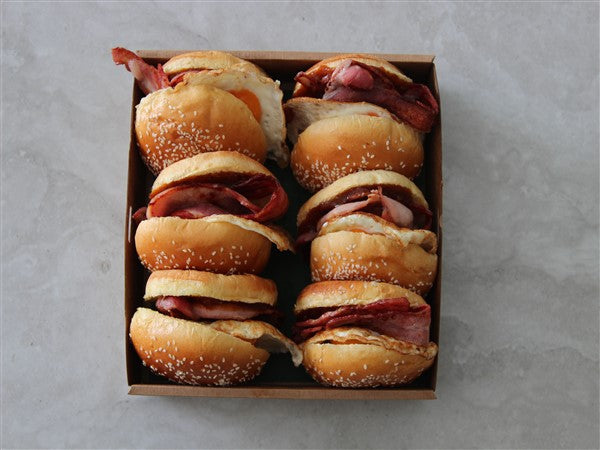 A box of bacon and egg rolls served on brioche buns with relish, foil-wrapped to retain heat.
