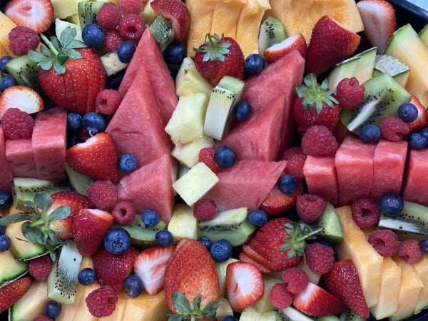 A bamboo tray filled with a beautifully arranged mixed fruit platter consisting of strawberries, blueberries, kiwi, watermelon, and pineapple.