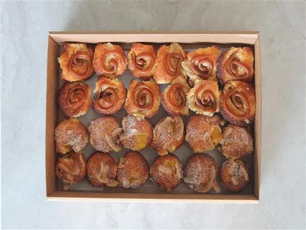 A top-down view of a light brown cardboard box filled with assorted baked mini muffins