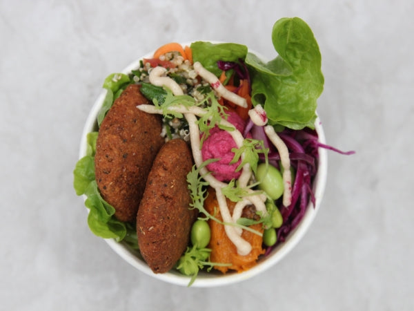 A pre-packaged salad bowl containing leafy greens, vegetables, and falafel, with dressing on the side.